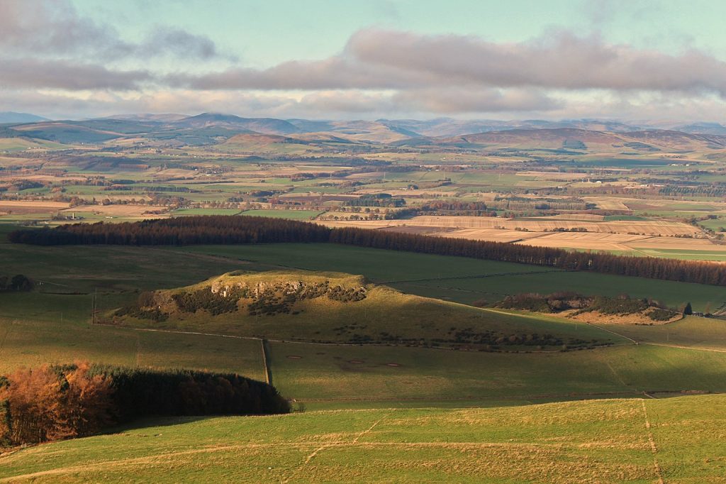 landscape with sunlit hillfort toward foreground, and mountains in the background